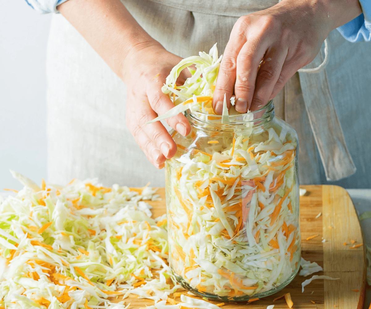 woman stuffing large jar with shredded cabbage and carrots to ferment sauerkraut