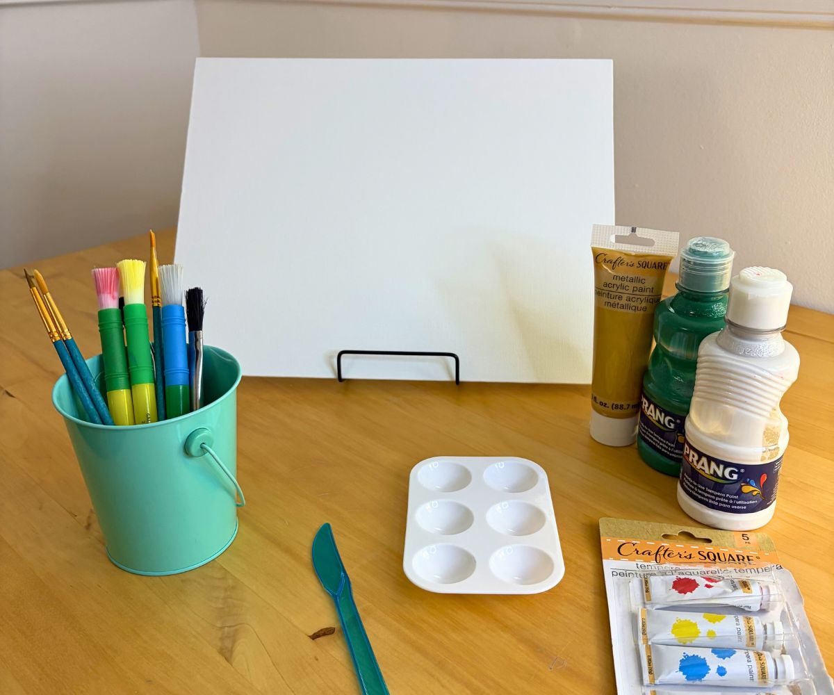 table with various paints, paintbrushes, canvas on a holder, etc.