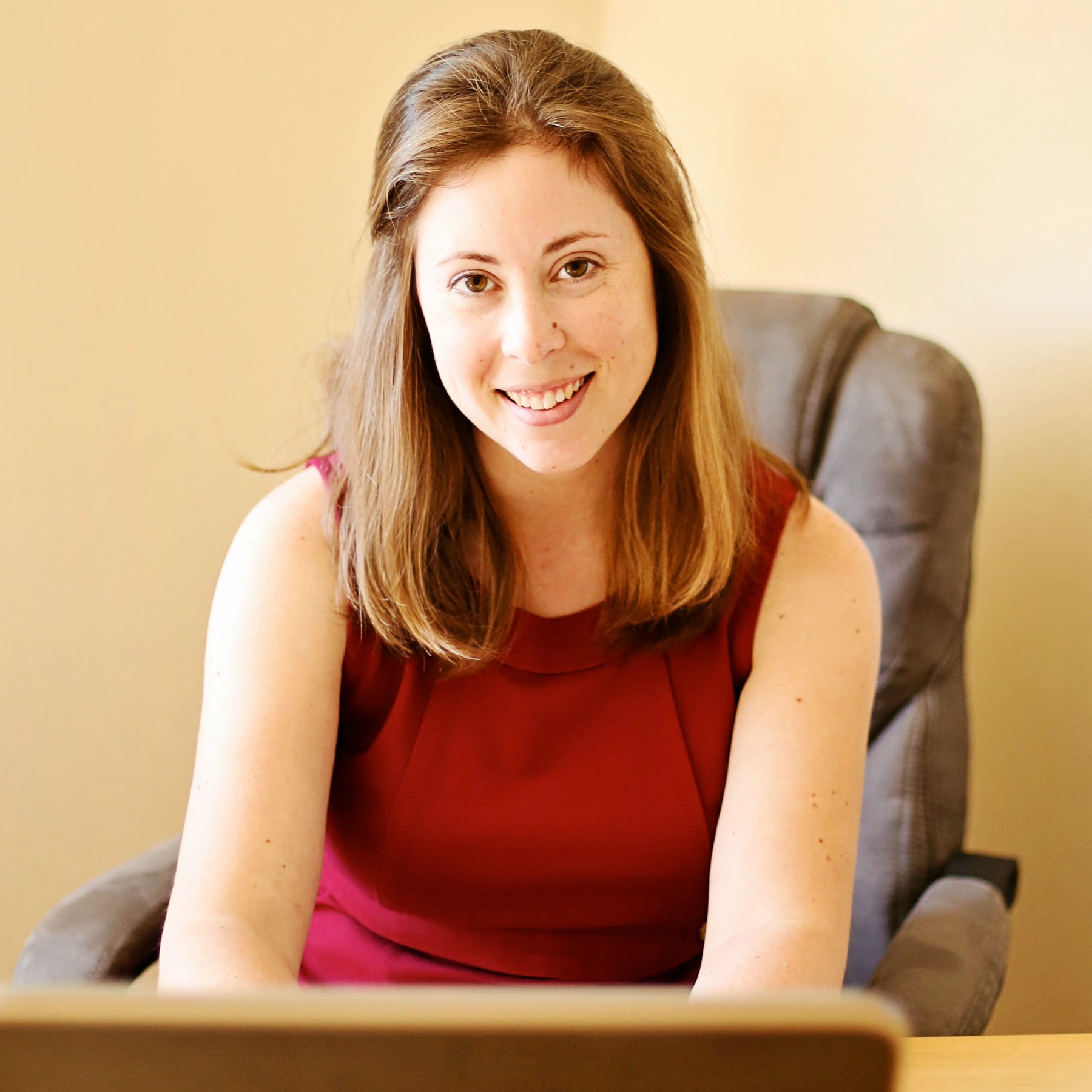 Amanda L. Grossman in red dress at desk with laptop
