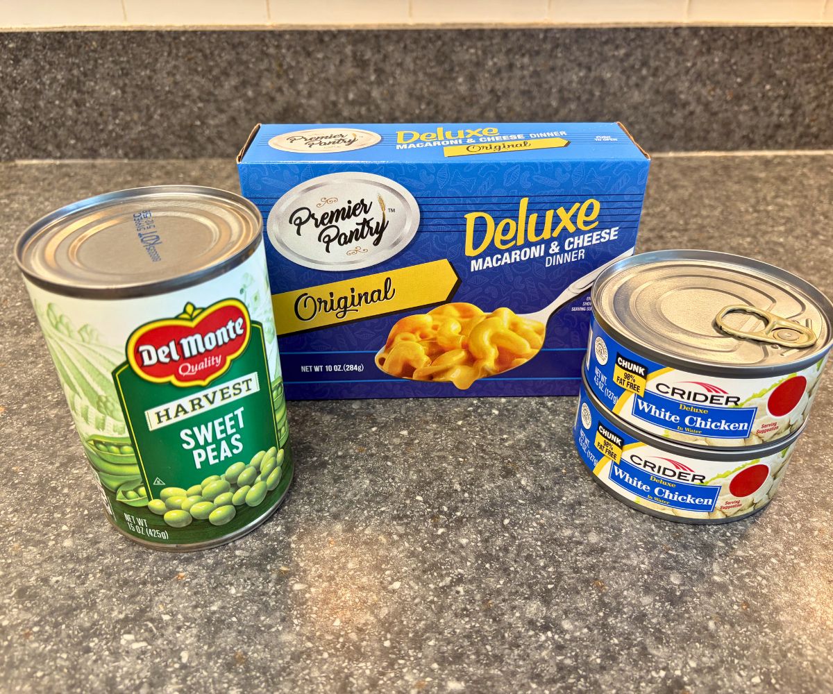 two cans of chicken, one can of sweet peas, and one box of macaroni and cheese dinner on counter