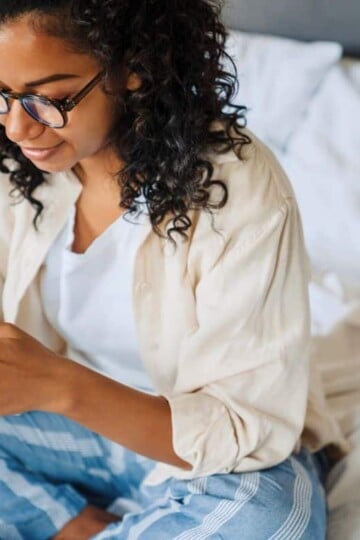 woman with curly hair on phone in bed, making money from home