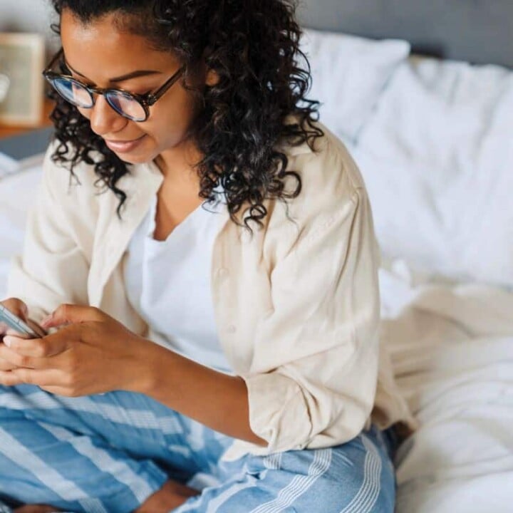 woman with curly hair on phone in bed, making money from home