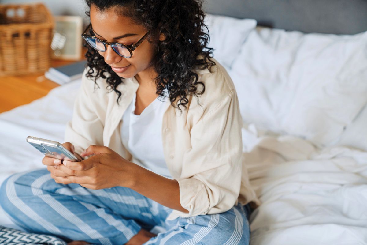 woman with curly hair on phone in bed, making money from home