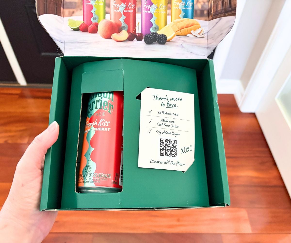 Amanda holding a hunter green box with a French Kiss Peach & Cherry flavored Maison Perrier drink inside