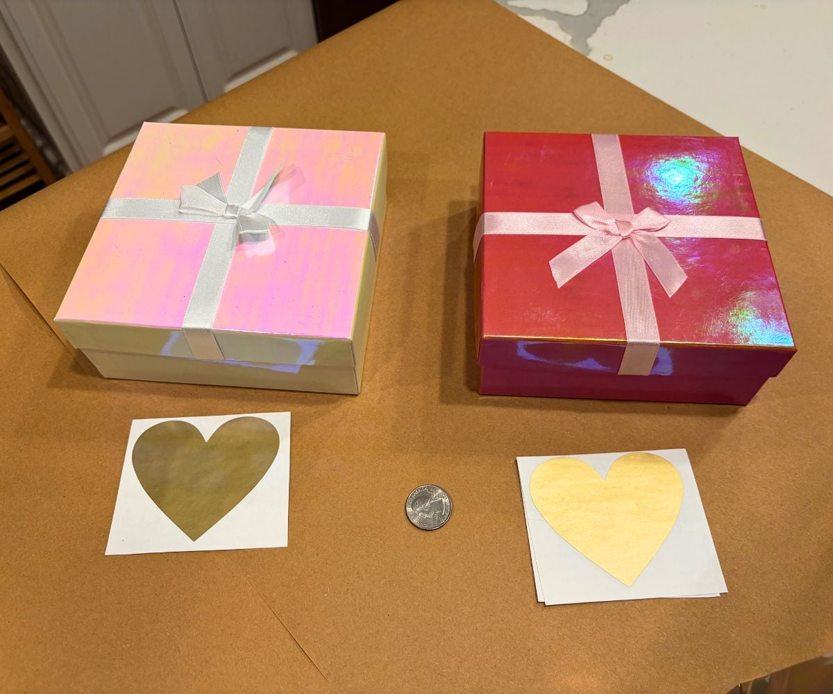 two pink colored small boxes, with two cards with a heart-shaped gold scratch off sticker on them and a quarter next to it, on butcher paper