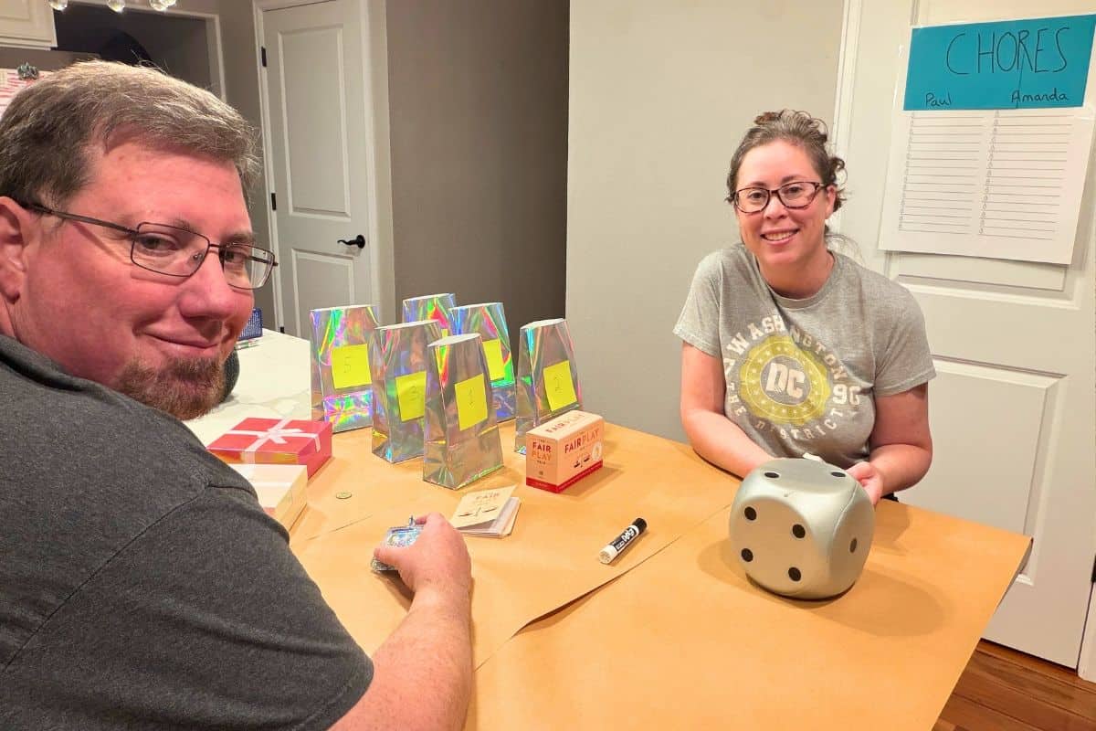 author and husband smiling at camera and about to roll dice to choose chore schedule for adults