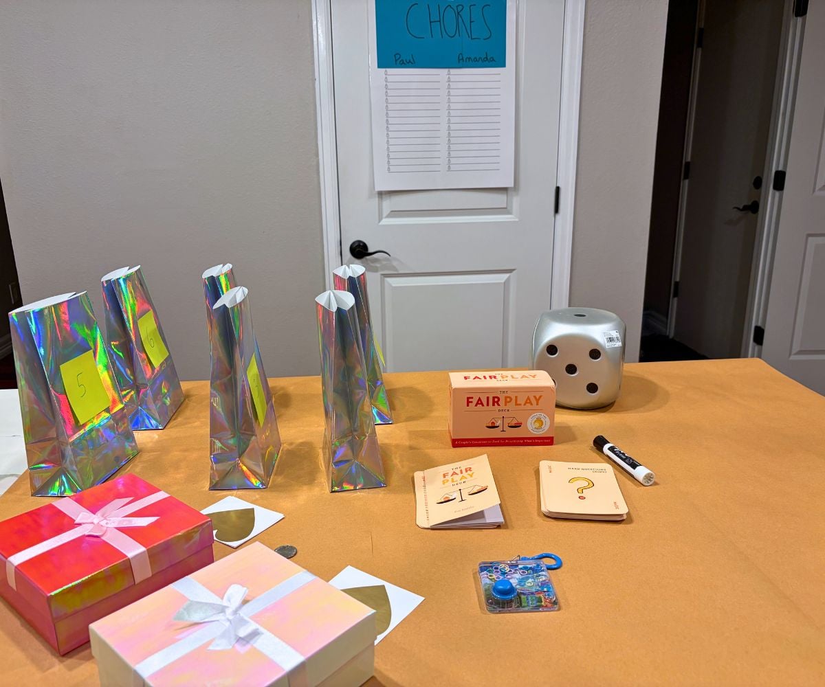 butcher paper covered table with colorful bags labeled 1-6, giant dice, Deck of Fair Play Cards, and pink boxes with scratch off heart cards